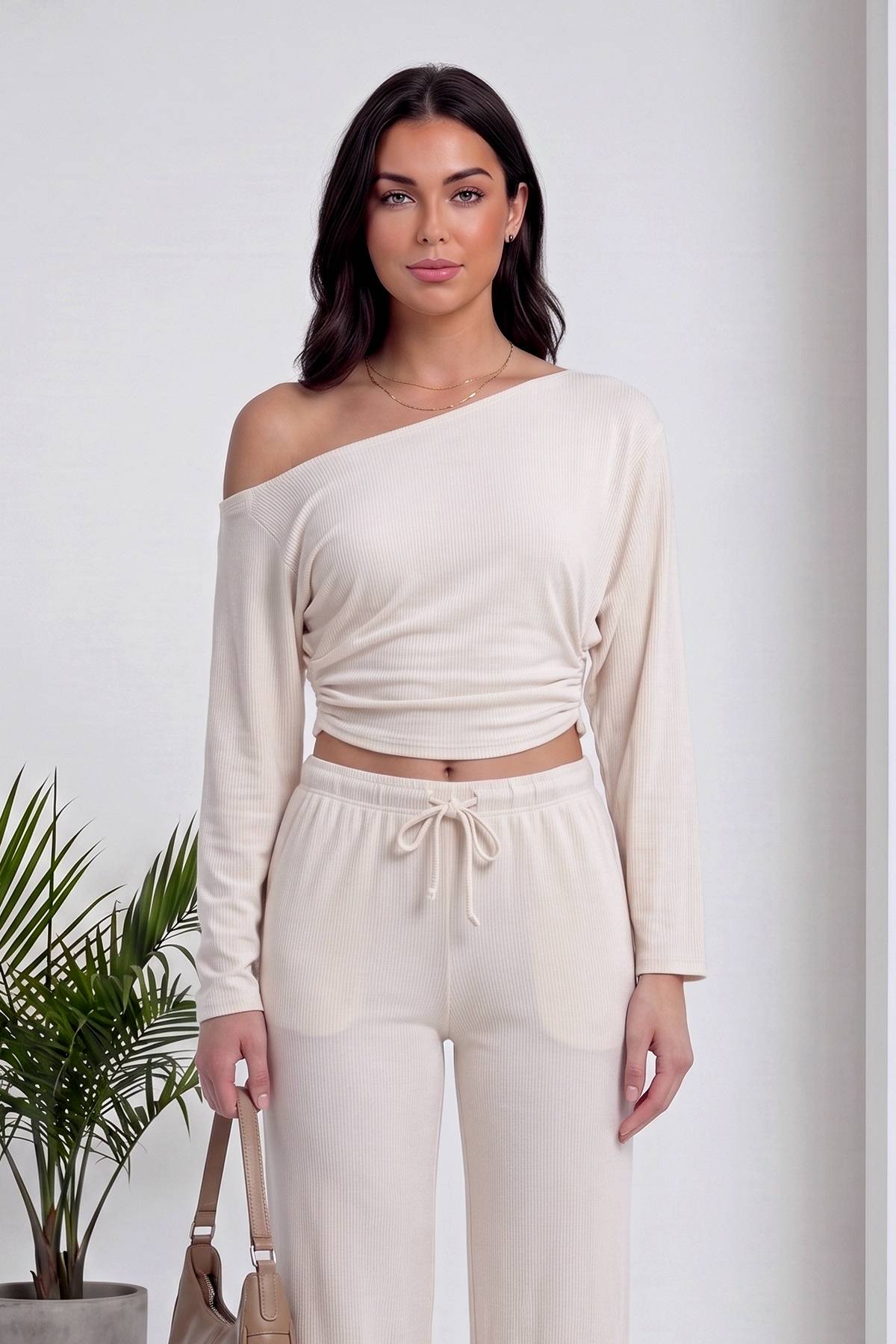 Modelin omuzdan kayan asimetrik yaka bej crop bluz ve büzgülü pantolon detayı