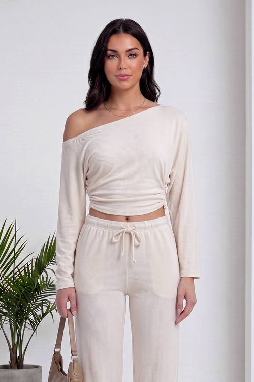 Modelin omuzdan kayan asimetrik yaka bej crop bluz ve büzgülü pantolon detayı