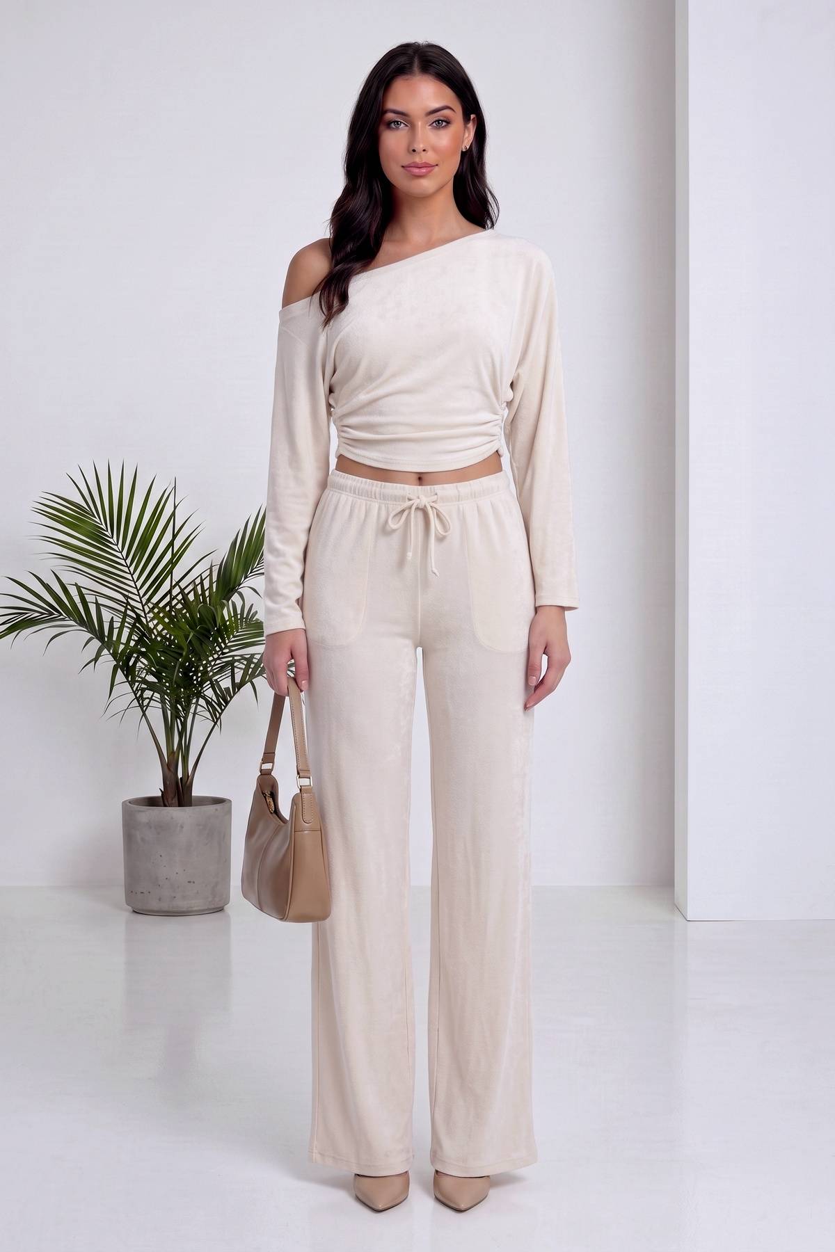 Modelin bej, asimetrik yaka, uzun kollu crop bluzu ve rahat kesim pantolonu tam görünüm
