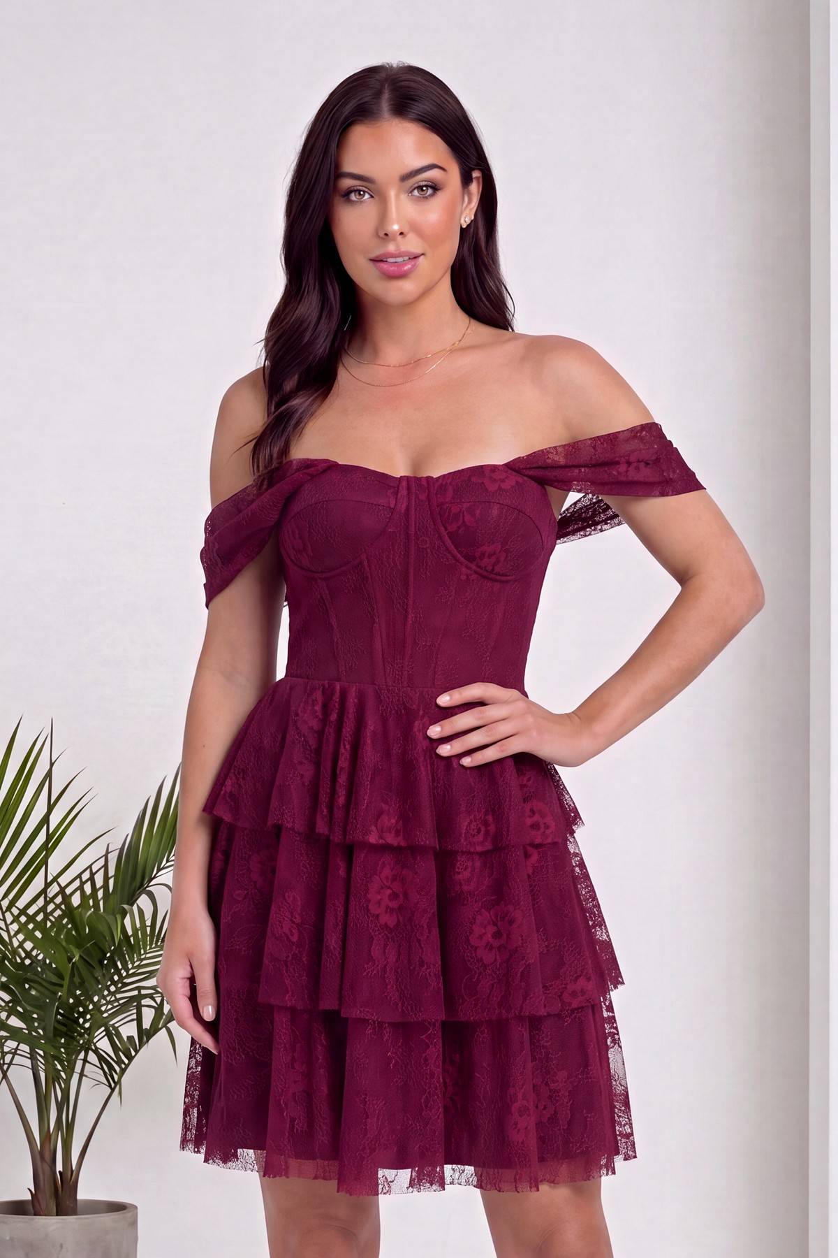 Bordo düşük omuzlu dantel mini abiye elbise, korsaj üst ve katmanlı etek detayı, modelin elini beline koyduğu yakın çekim