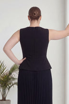 Siyah büyük beden piliseli kolsuz midi elbise ar, topuz saçlı, bir eli belinde çiçek önü.