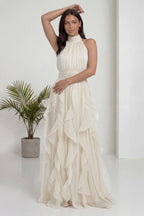 The ZKS ekru halter yaka fırfırlı uzun abiye elbise, sol eli belde, sağ kol havada poz