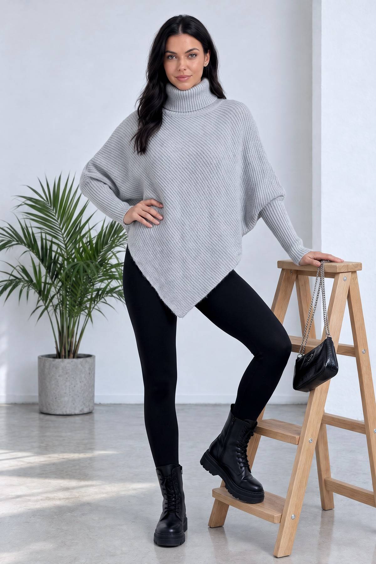 Model, The ZKS gri asimetrik boğazlı kazağını siyah tayt ve botlarla kombinleyerek poz veriyor.