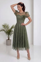 The ZKS haki balon kol abiye elbise, modelin elini saçına götürdüğü poz