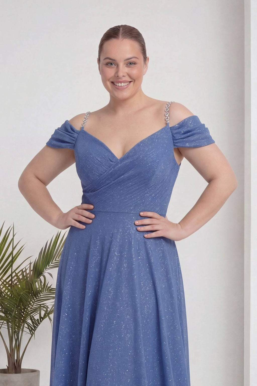 The ZKS indigo büyük beden kloş piliseli kruvaze abiye elbise, omuzları açık, V yaka, modelin gülümseyen yüzü