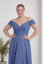 The ZKS indigo büyük beden kloş piliseli kruvaze abiye elbise, omuzları açık, V yaka, modelin gülümseyen yüzü