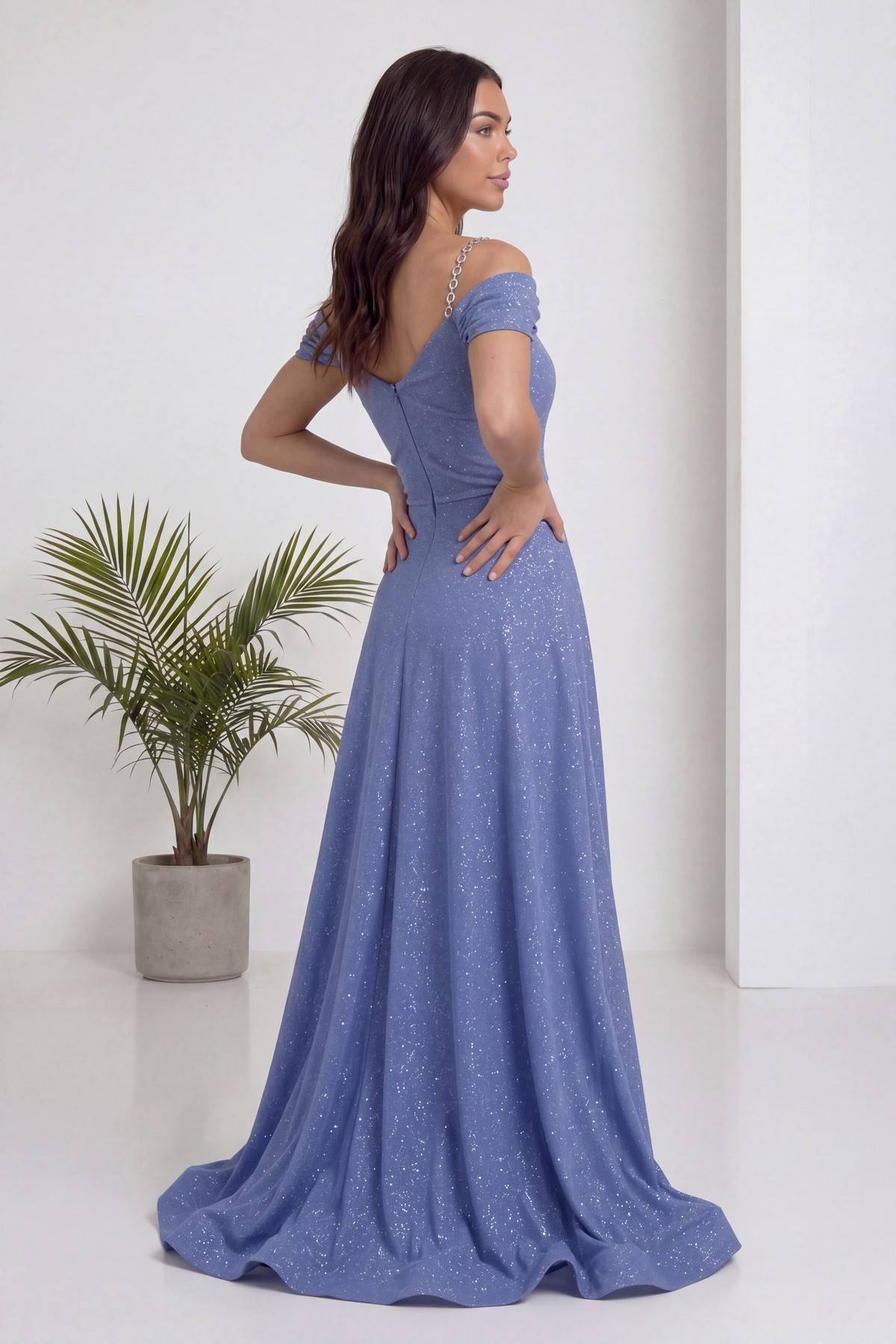 The ZKS indigo rengi, düşük omuzlu, simli, piliseli uzun abiye elbise, arka görünüm, model elleri belinde