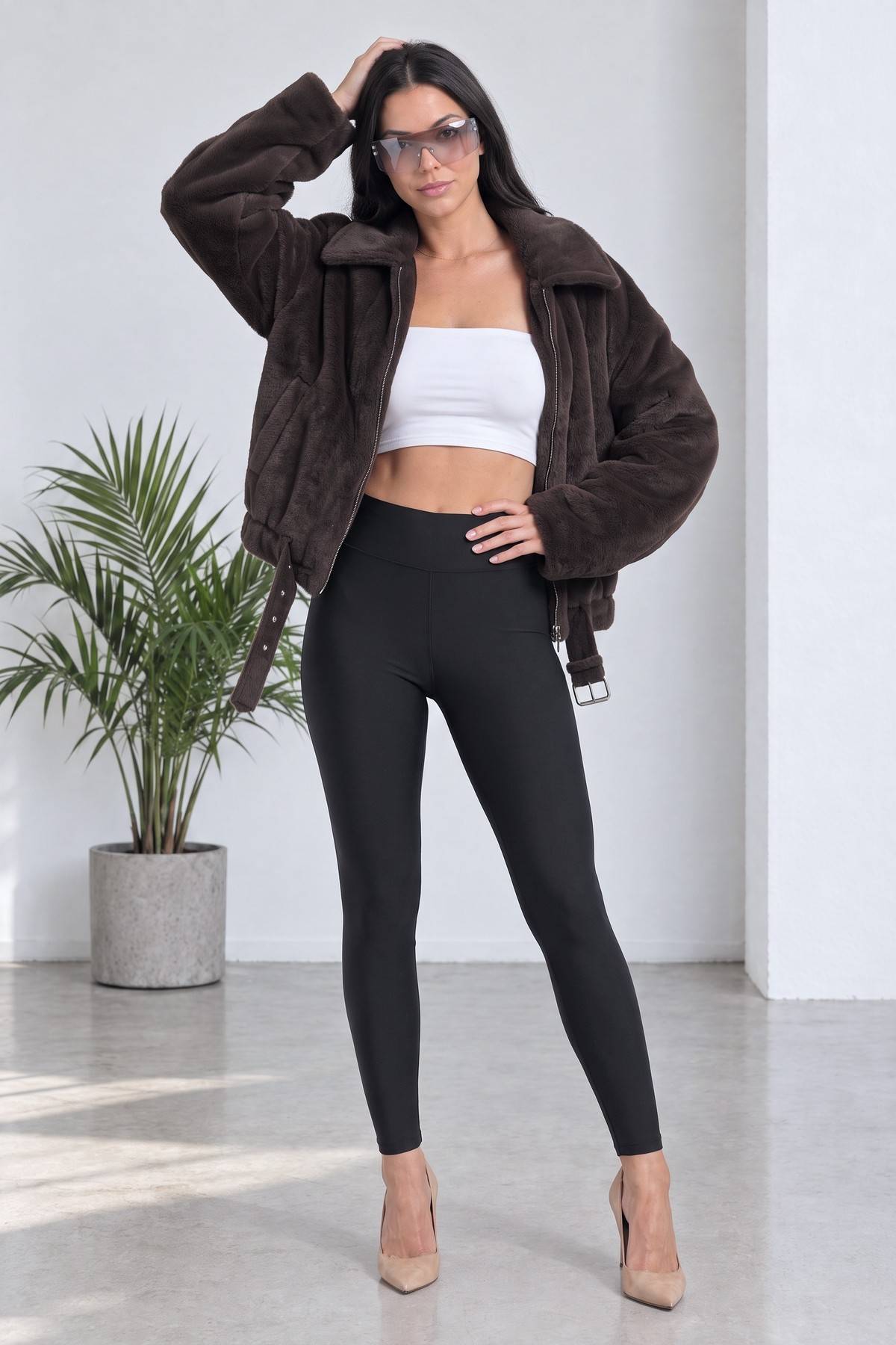 Model kahverengi bomber ceket ve beyaz crop top ile poz veriyor, arka plan bitki