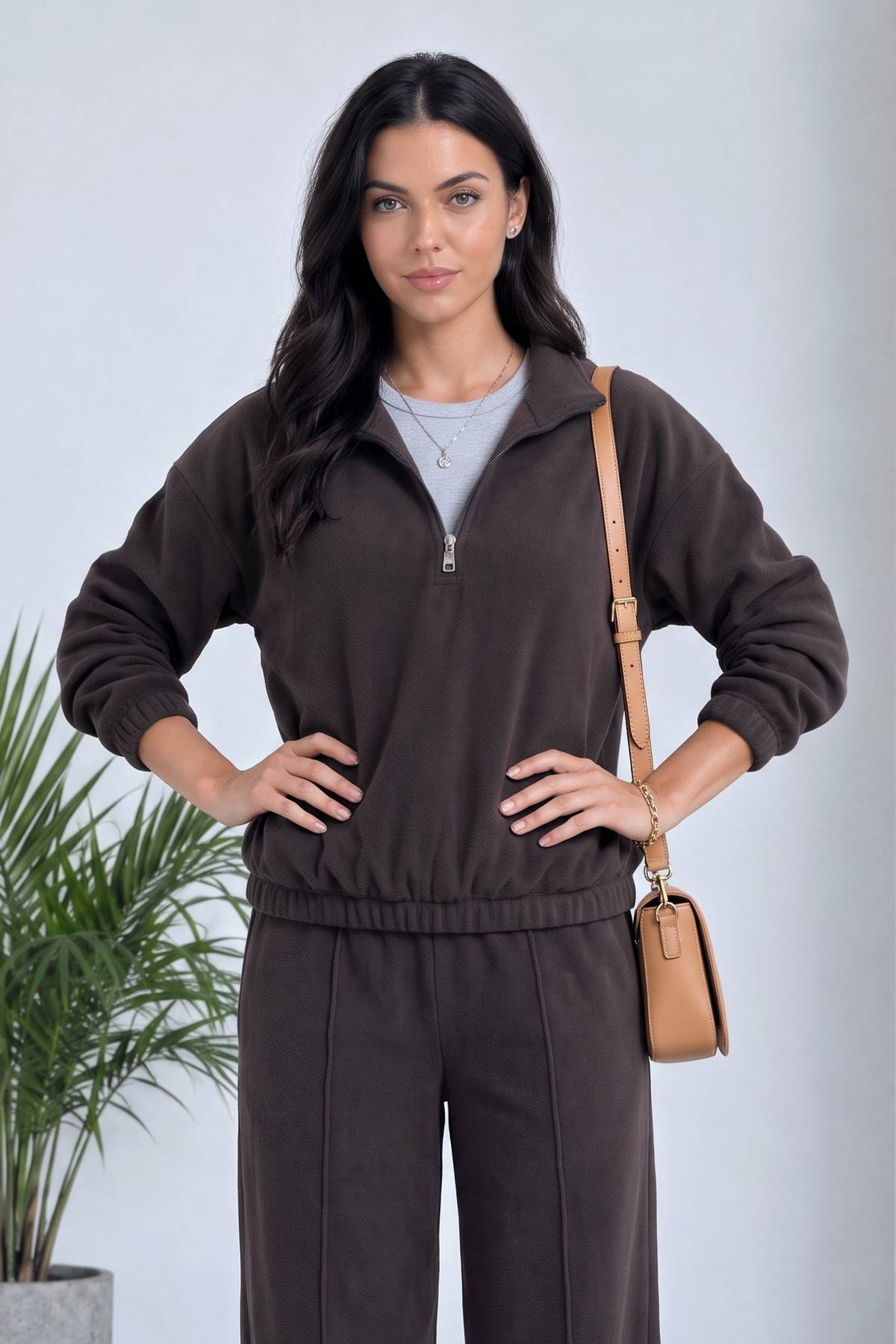 Model kahverengi ZKS takımın sweatshirtü ve geniş paça pantolonuyla hafifçe gülümsüyor