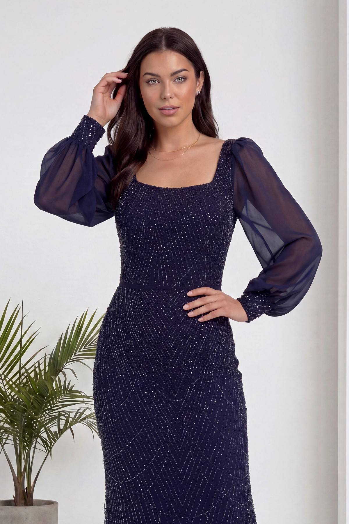 Lacivert kare yaka şifon kollu, balık kesim, işlemeli abiye elbise modelin eli saçında poz verirken