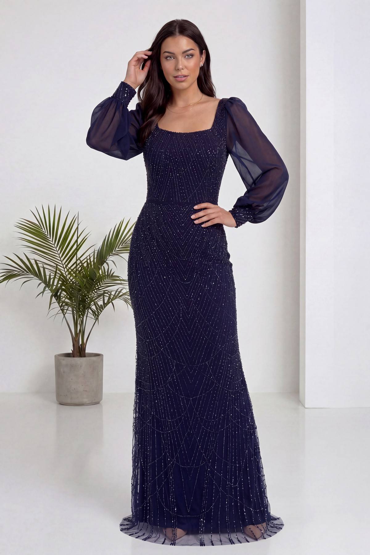 Lacivert kare yaka şifon kollu, balık kesim, işlemeli abiye elbise modelin elini saçına götürdüğü poz