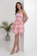 Pudra straplez elbise, fırfırlı kısa etek ve fiyonk detayıyla duvara yaslanmış model