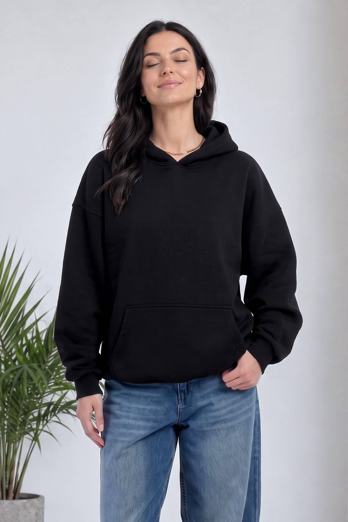 The ZKS siyah kapüşonlu sweatshirt, ön cep detayı, modelin beli bükülmüş duruşu