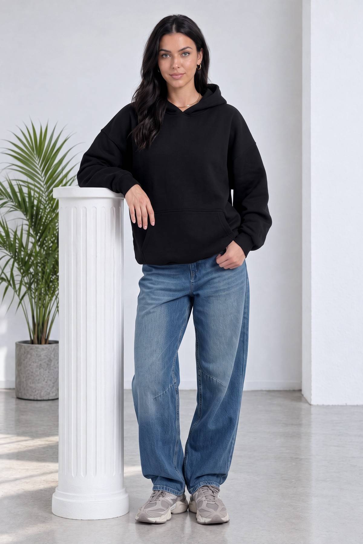 The ZKS siyah kapüşonlu sweatshirt, model bir sütuna yaslanmış, geniş paça kot pantolon ile