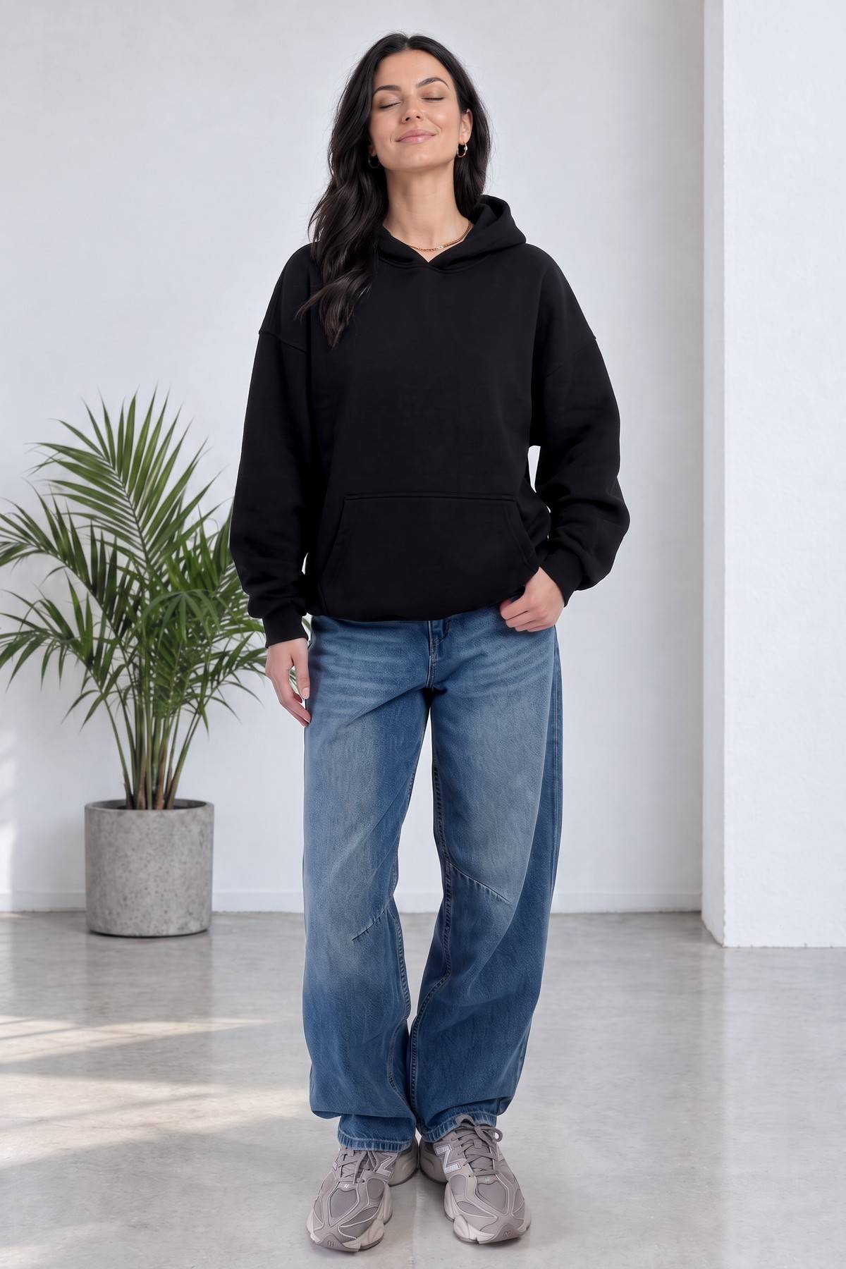 Model, The ZKS siyah kapüşonlu sweatshirt ve geniş paça kot pantolon ile ayakta duruyor
