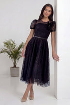 Model, The ZKS siyah dantel midi elbisesiyle duvara yaslanmış, zarif bir duruş sergiliyor