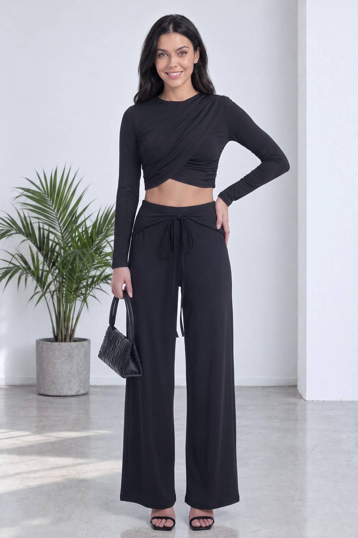 The ZKS siyah crop bluz ve geniş paça pantolon takımı elinde çanta ile tam duruş pozu