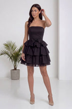 Model, The ZKS straplez siyah fırfır etekli kısa abiye elbiseyi arkadan gösteriyor, fermuar detayı ve katmanlı etek belirgin.