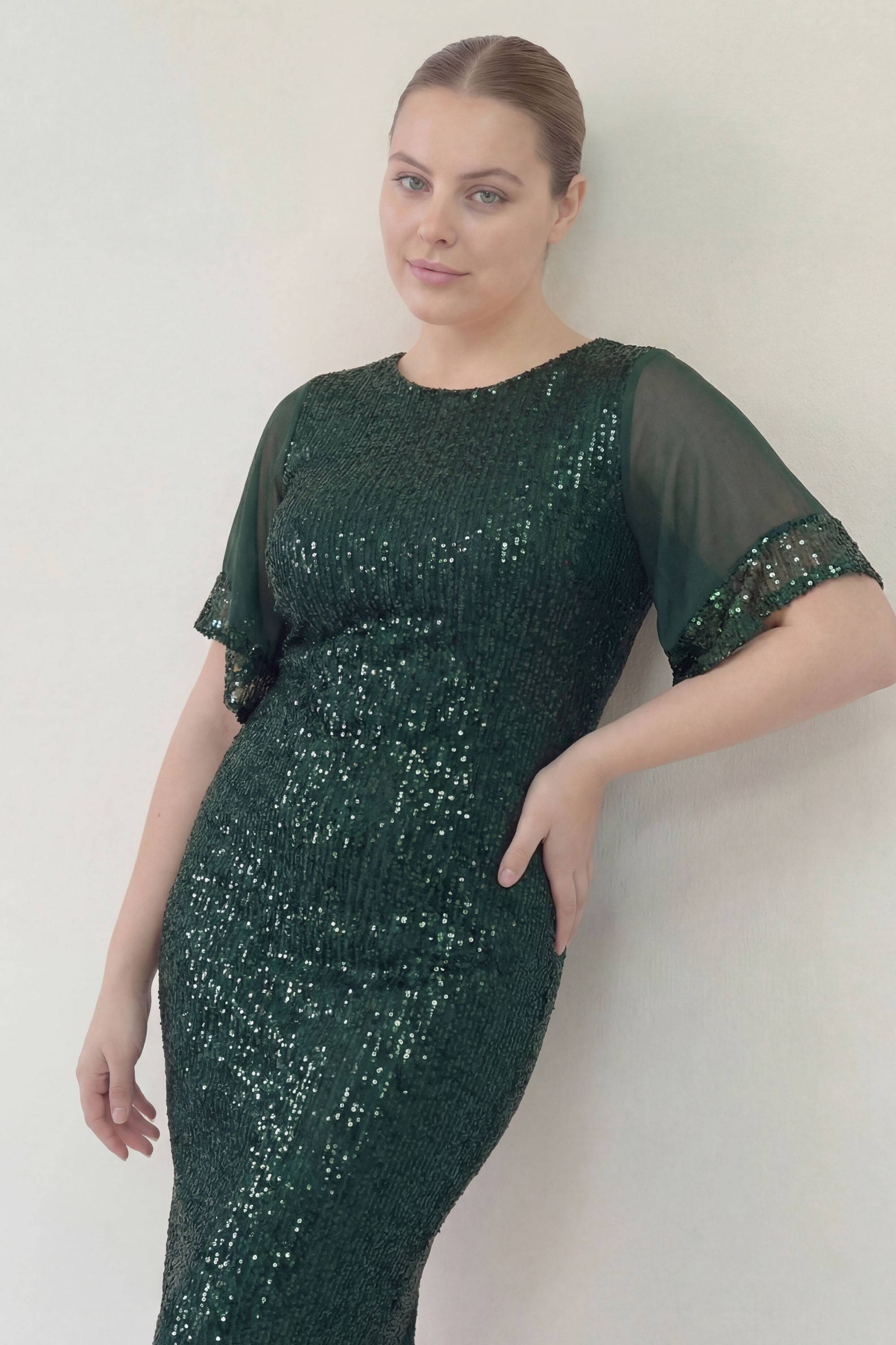 ZKS büyük beden yeşil pulpayet midi abiye elbise, şeffaf kollu, duvara yaslanmış şık poz