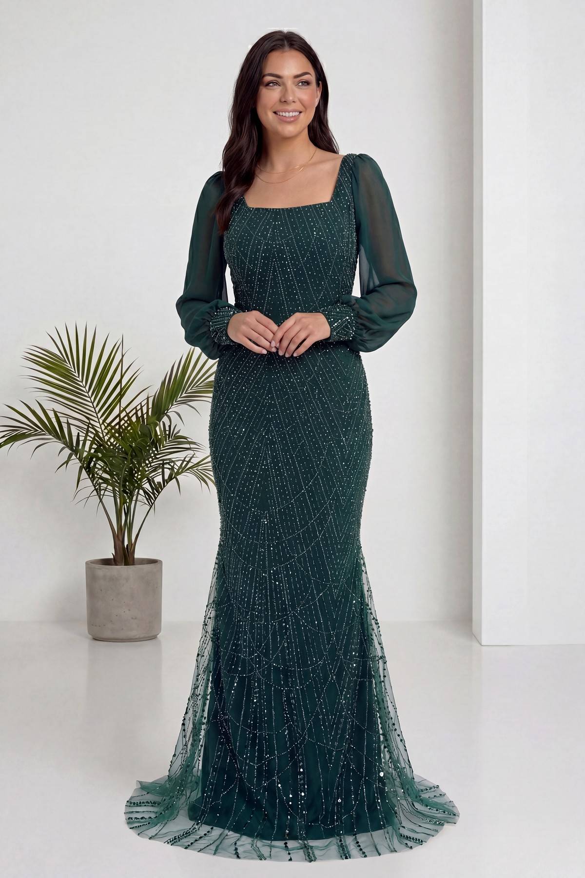 The ZKS yeşil kare yaka şifon balık abiye, ön cepheden elleri belinde zarif bir poz